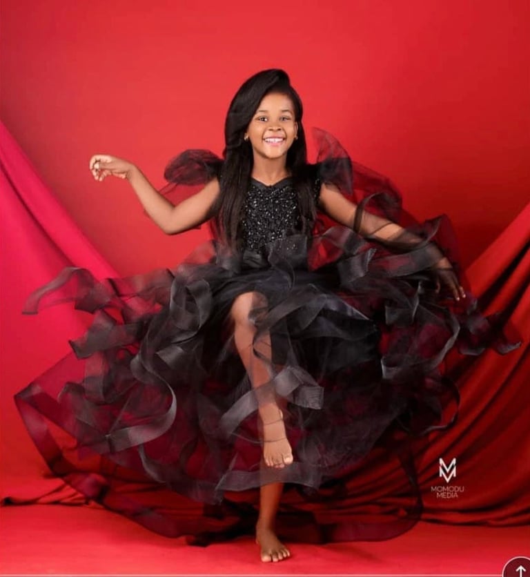 Young girl in black sequined dress with burgundy tulle skirt posing against red background