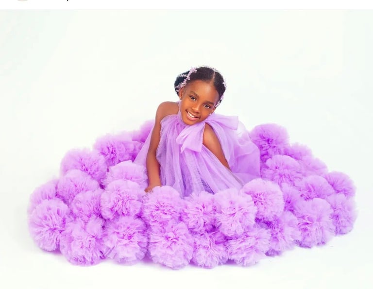 Young girl in lavender tulle dress surrounded by purple tulle pom-poms against white background