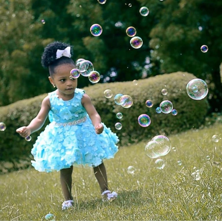 Young child in blue dress playing with soap bubbles outdoors in a grassy garden area