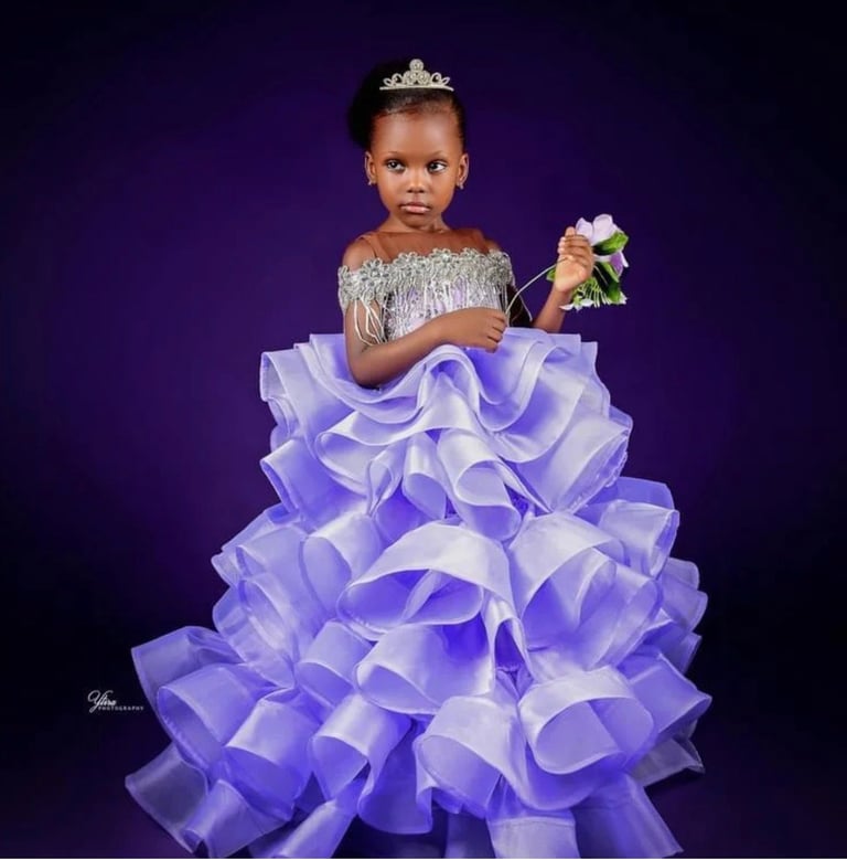 Young girl in lavender pageant gown with ruffled skirt, tiara, and bouquet against purple background